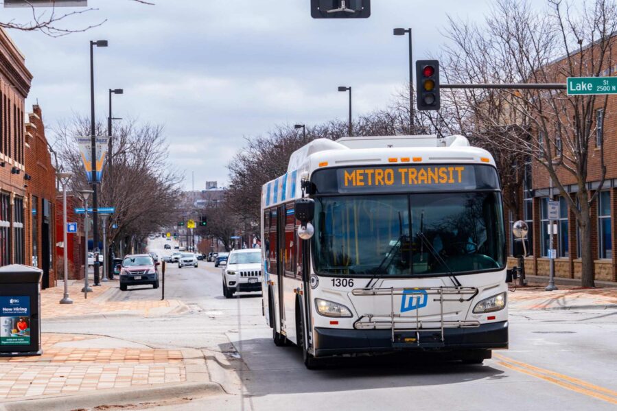 A white with blue stripes Metro bus goes down 24th street near Lake